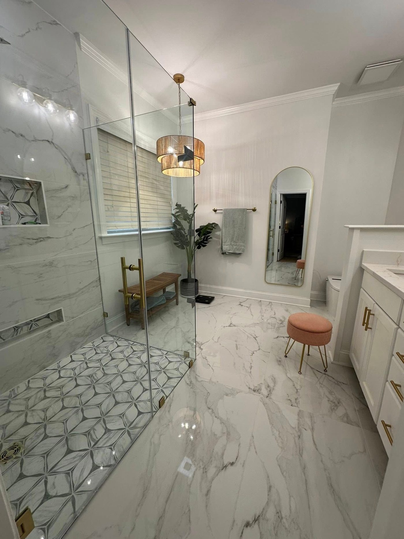 Bright marble bathroom remodel with arched mirror and brass fixtures by Beast Mode Remodeling